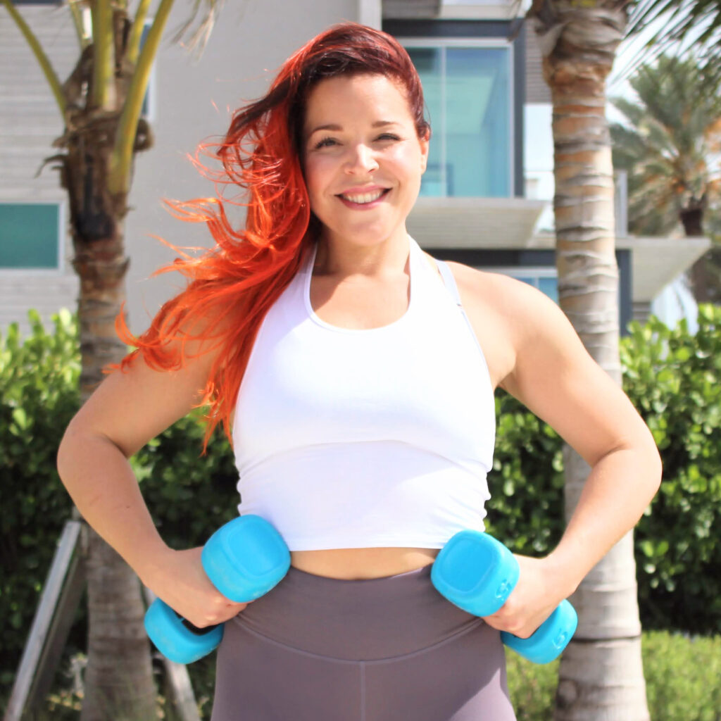 Gwen, FIT by GP strength coach for women 40+, holding weights and smiling outdoors in Miami