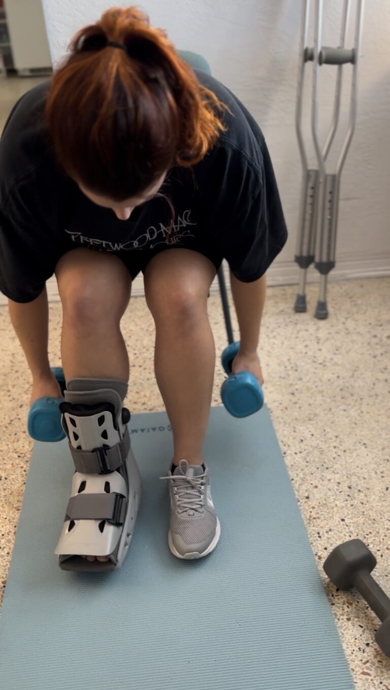 Gwen training with a dumbbell while wearing a walking boot, crutches nearby – FIT by GP, adapting through injury