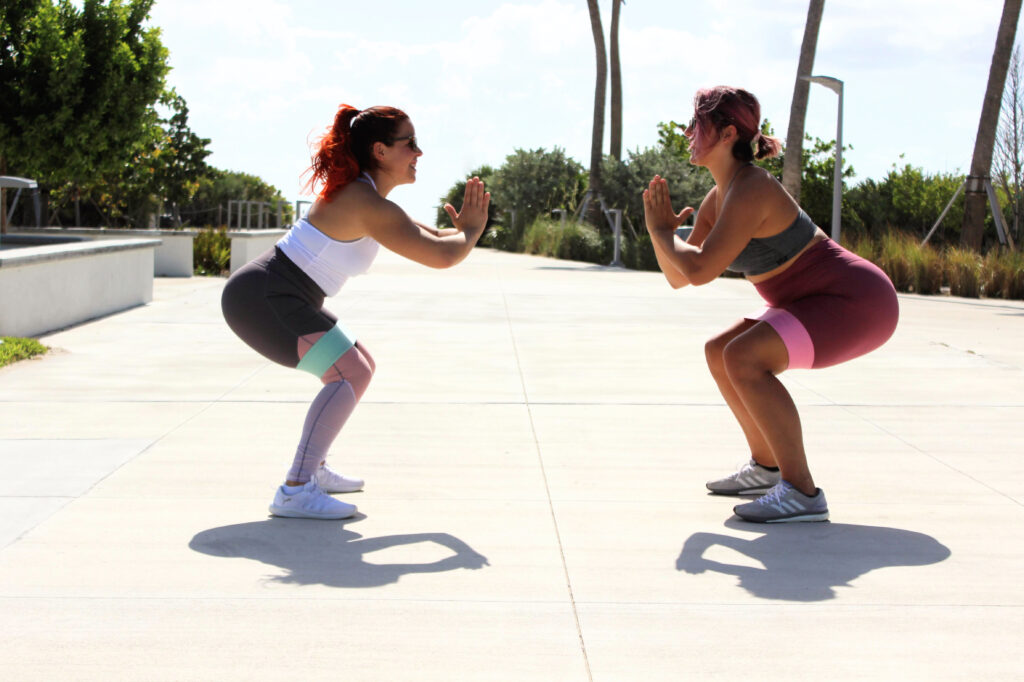 Two women doing banded squats together outdoors – FIT by GP live classes for women 40+