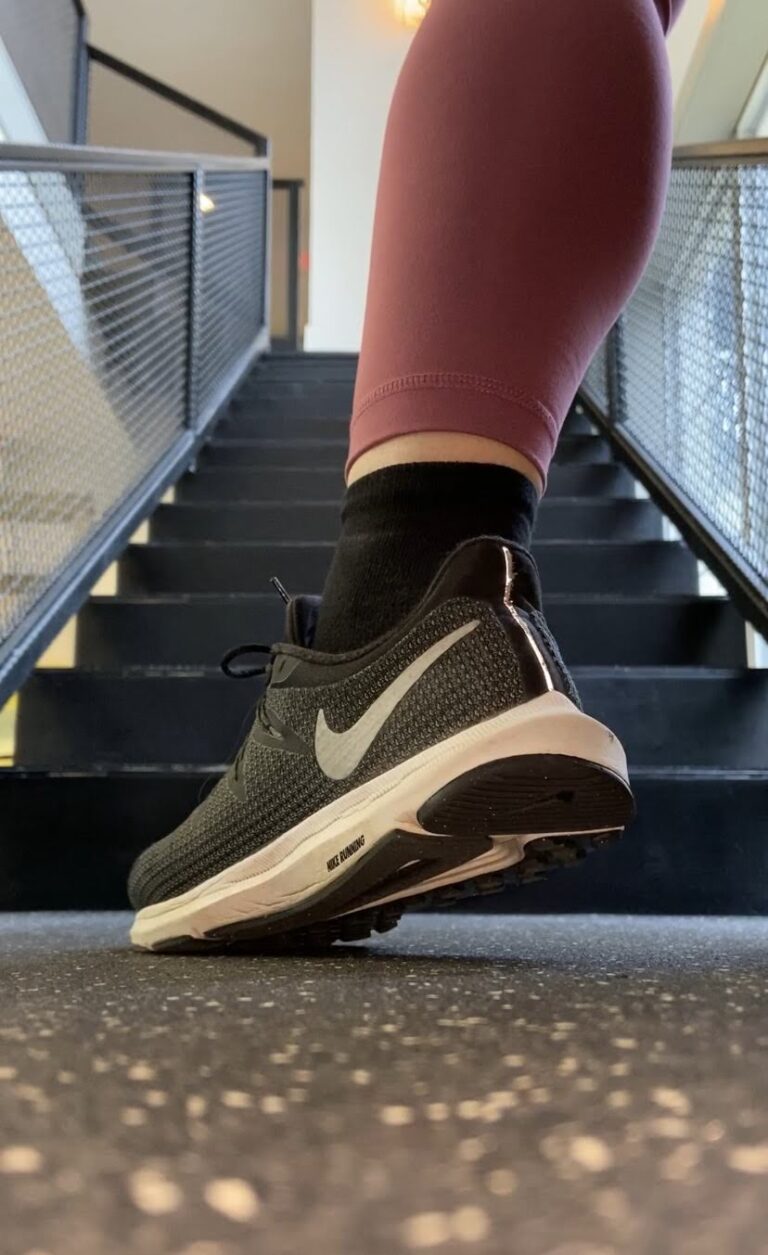 Woman in maroon leggings and black sneakers taking a step up a staircase — a small step that counts.